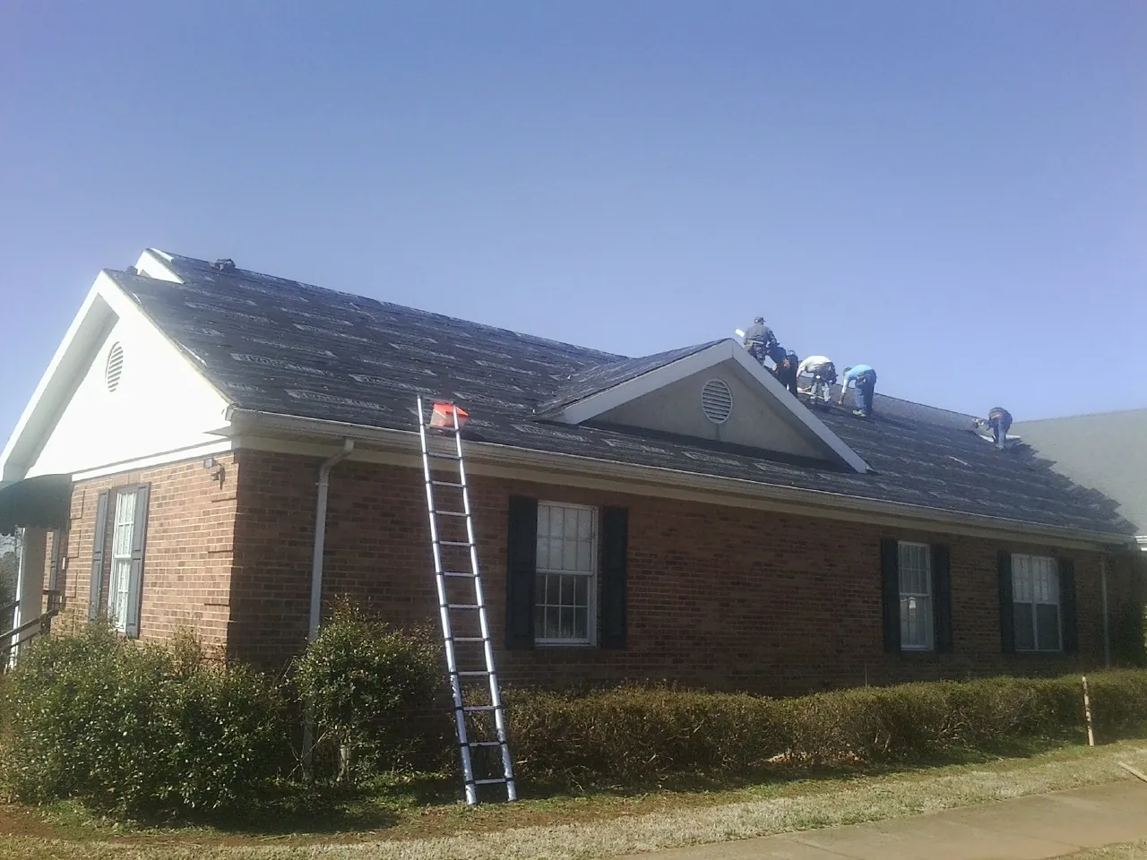 Crew tearing shingles off a brick ranch roof with a ladder set — Emergency Roof Repair work by our crew in Schodack Landing