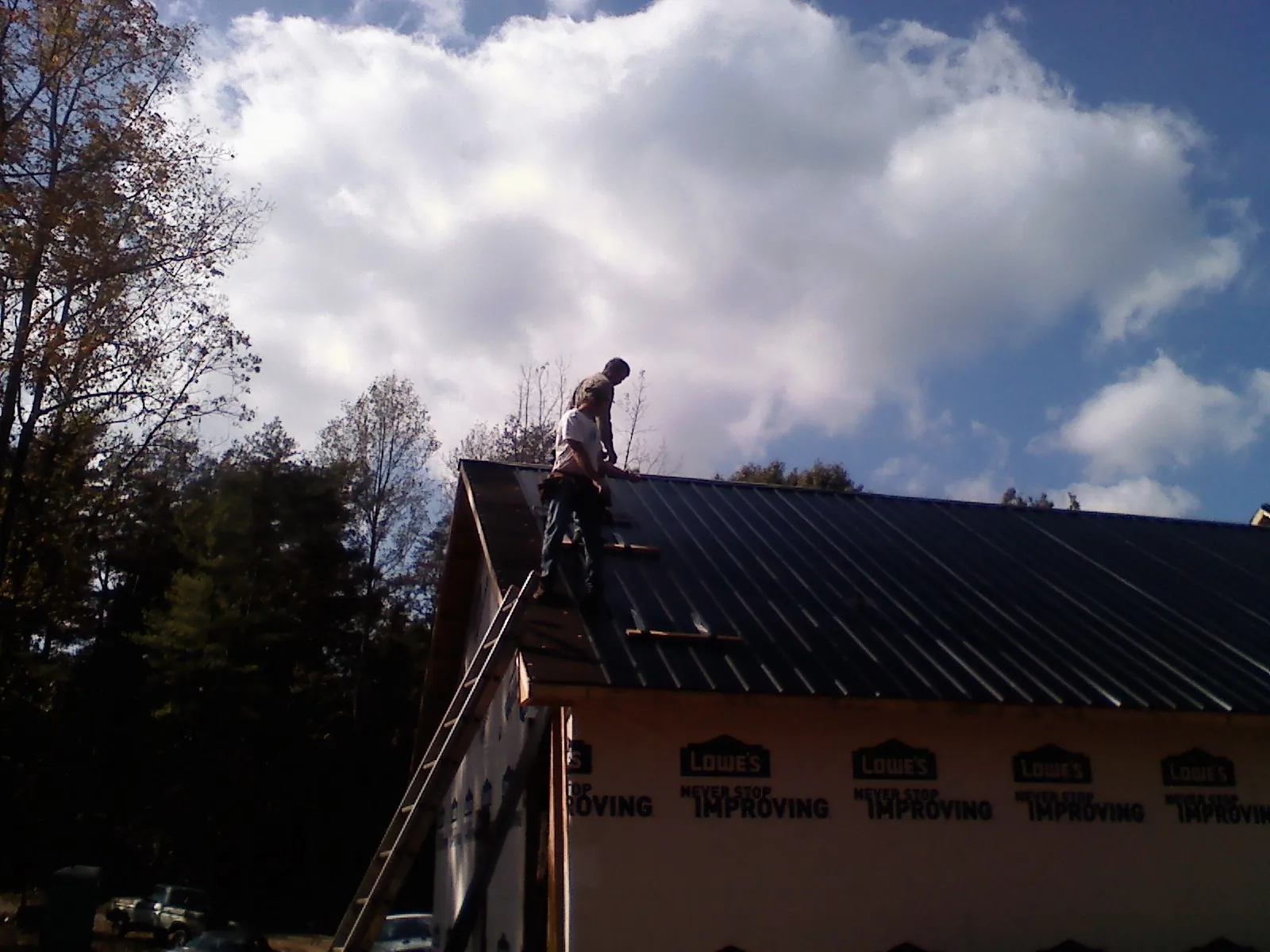 Roofer fastening dark metal panels high against a cloudy sky, from a Roof Inspection job in Schodack Landing
