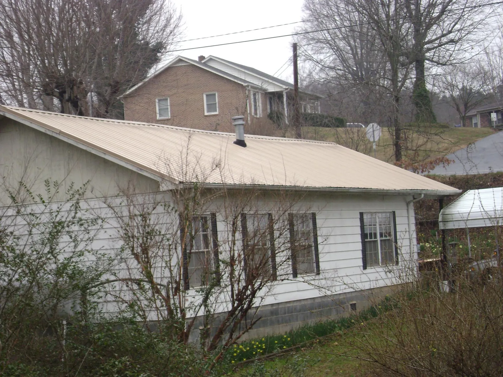 Tan metal roof on a white sided house set into a hillside — Commercial Roofing by Roofing Brothers in Schodack Landing